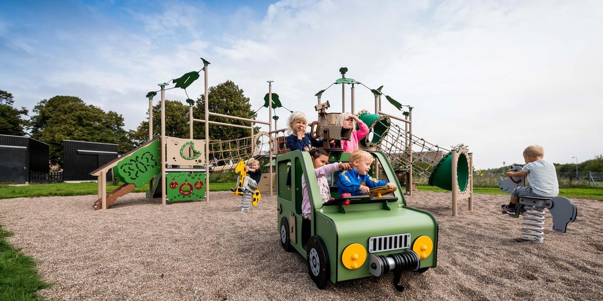 Playground with a green car on which many children are sitting